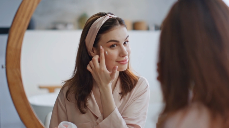 Žena nanosi kremu na lice ispred ogledala